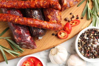 Photo of Different smoked sausages, rosemary and spices on white marble table, flat lay