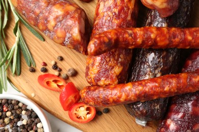 Photo of Different smoked sausages, rosemary and spices on white table, flat lay