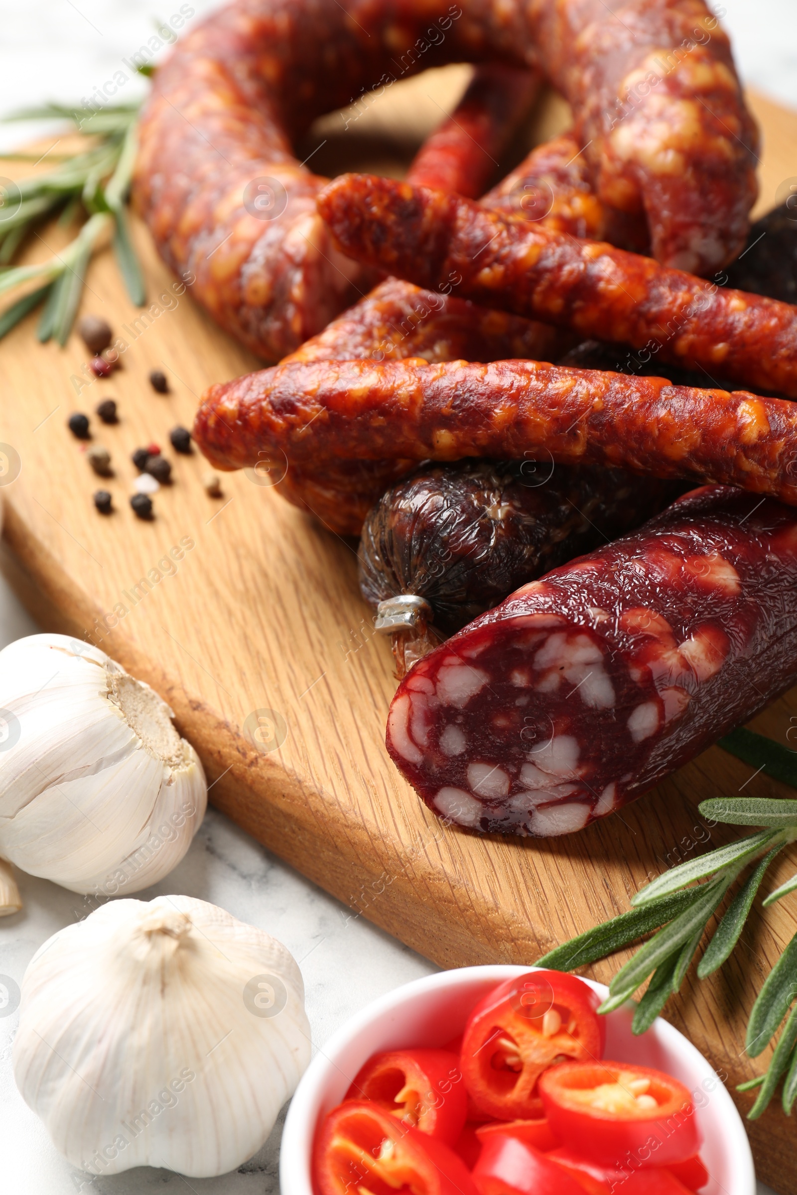 Photo of Different smoked sausages, chili pepper and garlic on white table, closeup