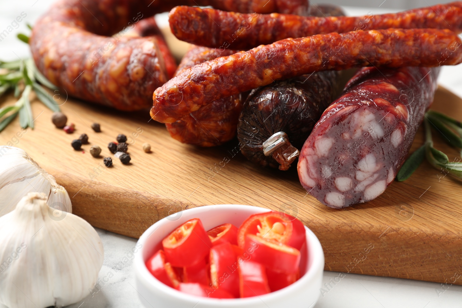 Photo of Different smoked sausages, chili pepper and garlic on white table, closeup