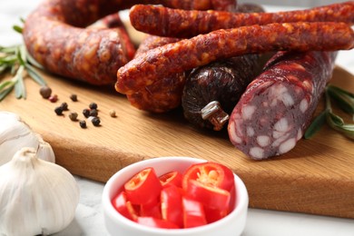 Photo of Different smoked sausages, chili pepper and garlic on white table, closeup