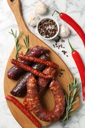 Photo of Different smoked sausages, rosemary and spices on white marble table, flat lay