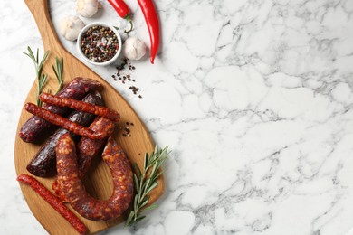 Photo of Different smoked sausages, rosemary and spices on white marble table, flat lay. Space for text