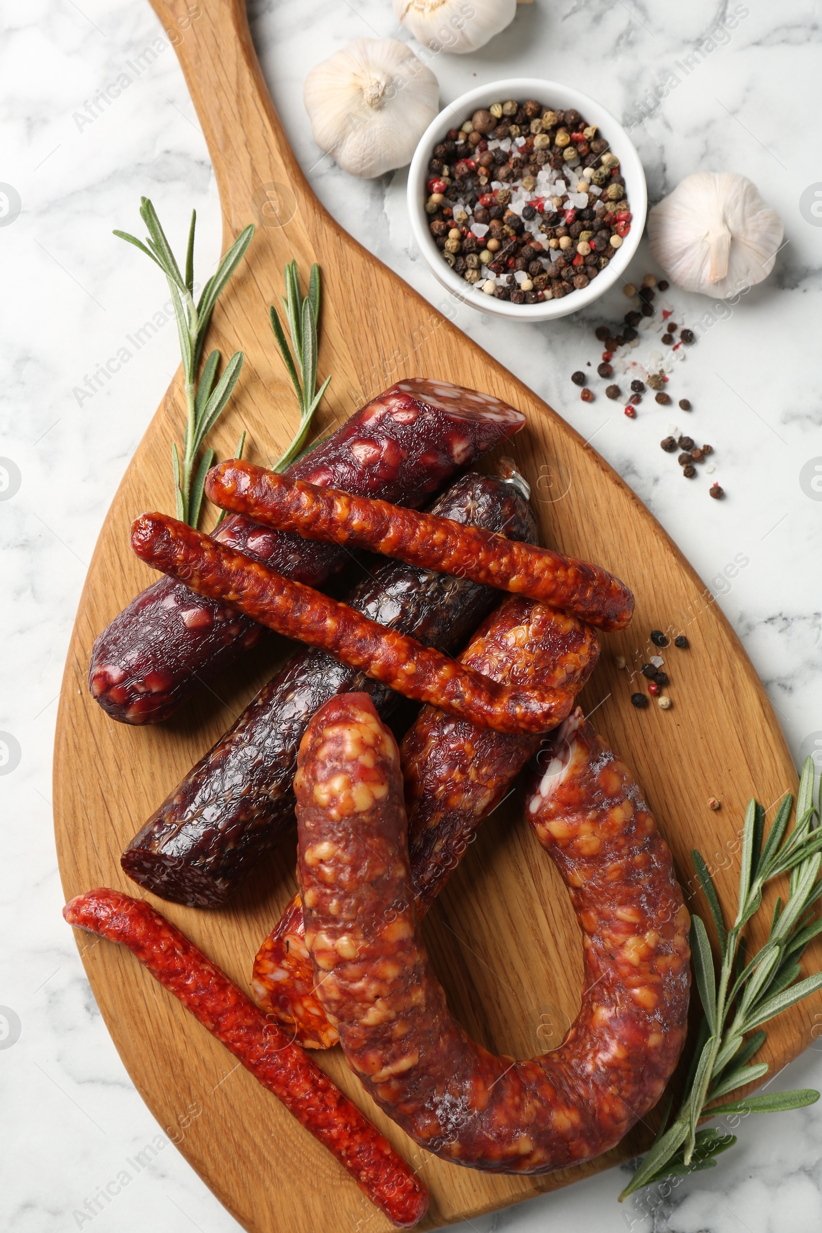 Photo of Different smoked sausages, rosemary and spices on white marble table, flat lay