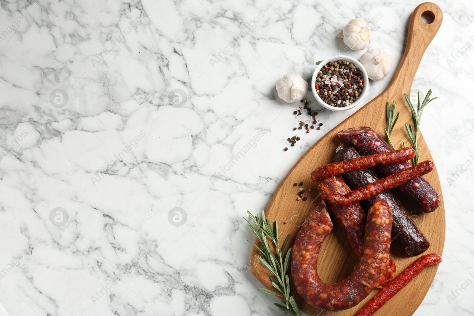 Photo of Different smoked sausages, rosemary and spices on white marble table, flat lay. Space for text