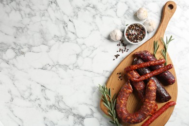 Photo of Different smoked sausages, rosemary and spices on white marble table, flat lay. Space for text