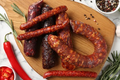 Photo of Different smoked sausages, rosemary and spices on white marble table, flat lay