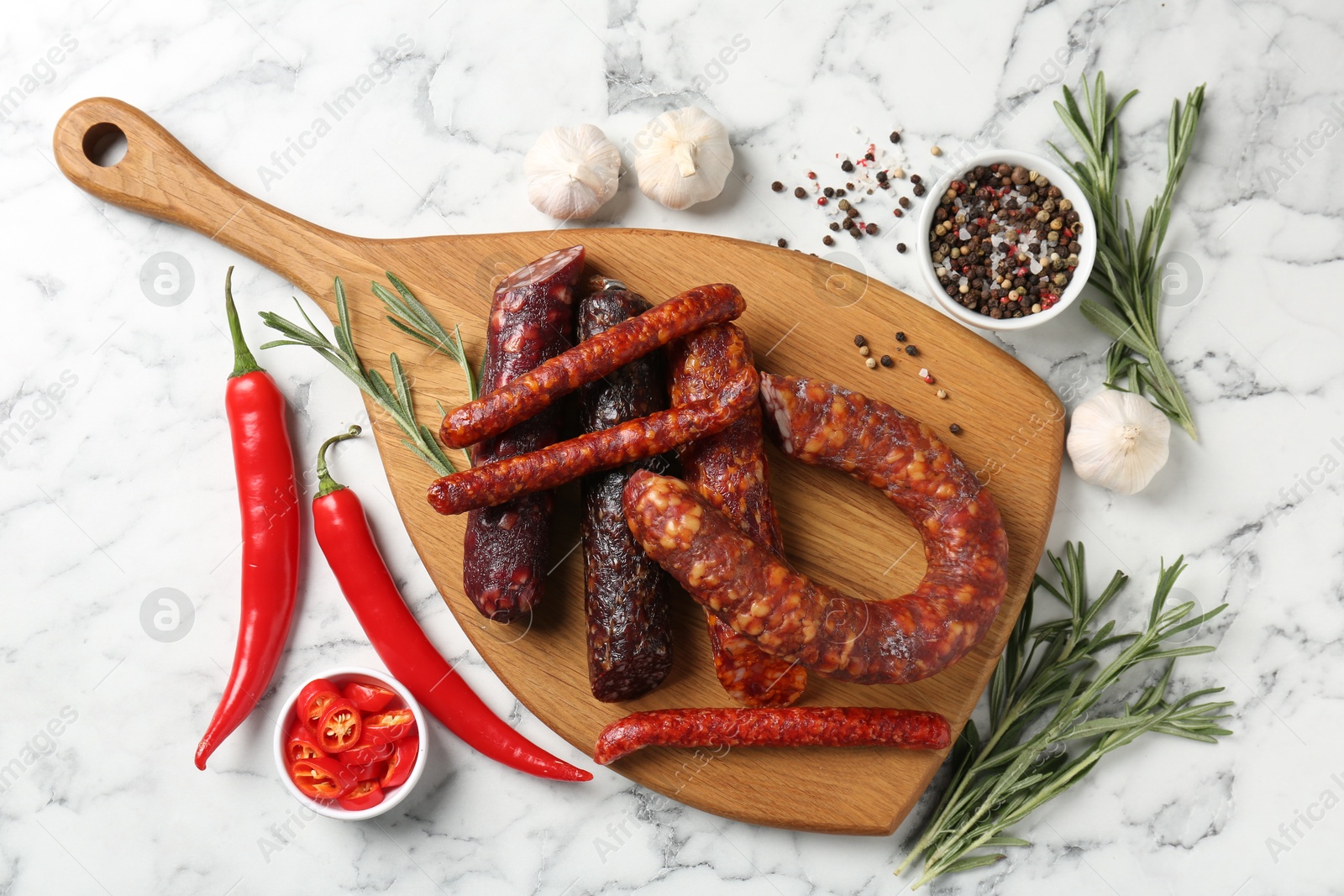 Photo of Different smoked sausages, rosemary and spices on white marble table, flat lay