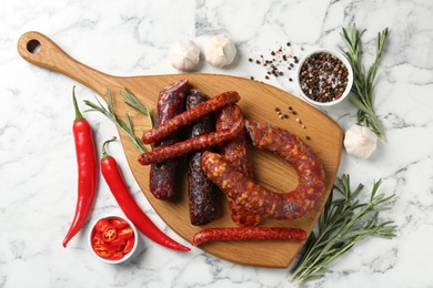 Photo of Different smoked sausages, rosemary and spices on white marble table, flat lay