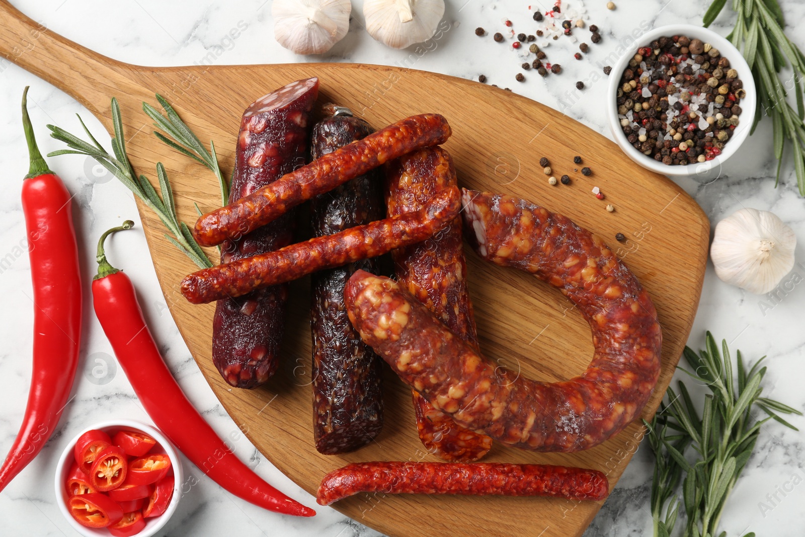 Photo of Different smoked sausages, rosemary and spices on white marble table, flat lay