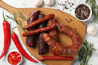 Photo of Different smoked sausages, rosemary and spices on white marble table, flat lay