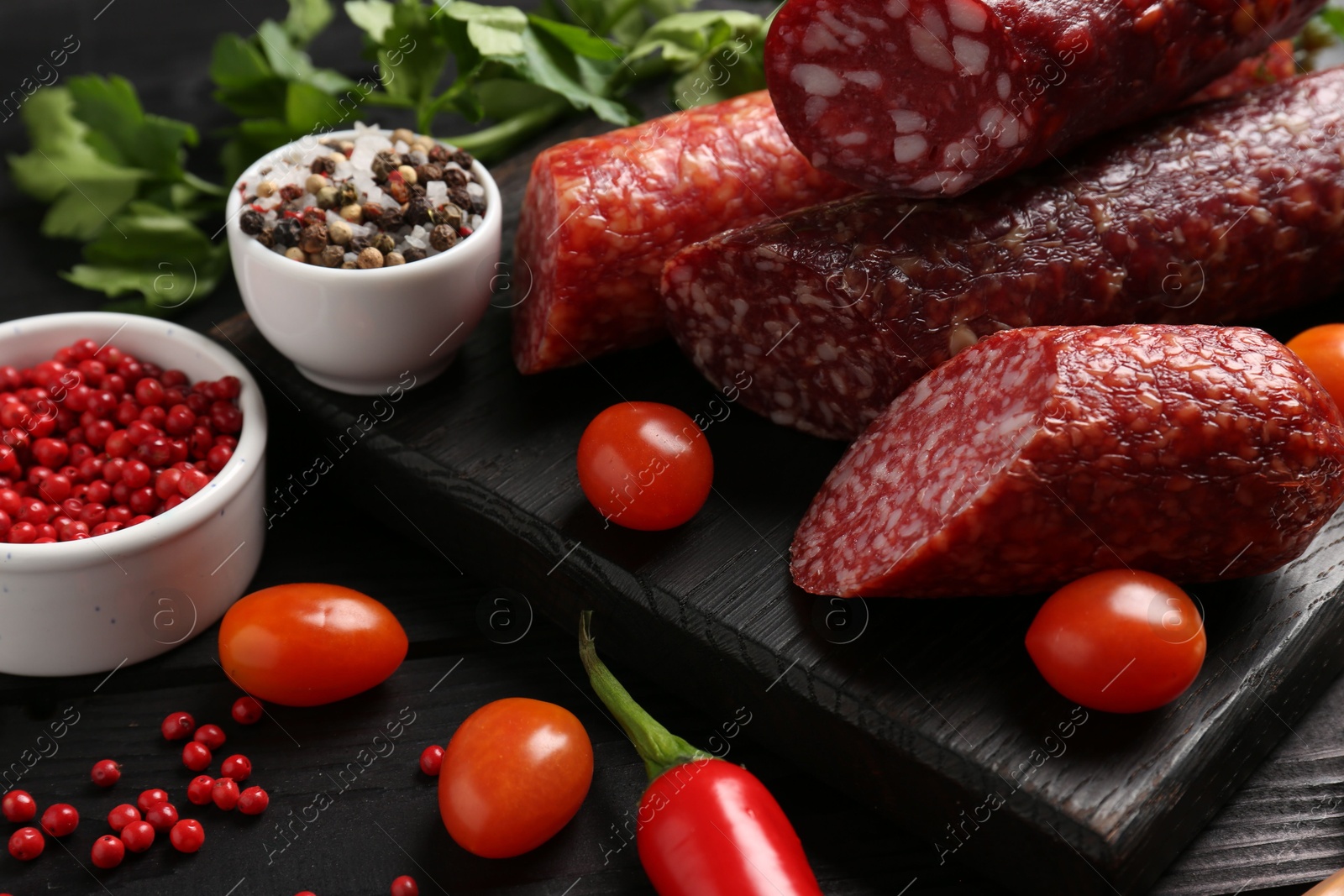 Photo of Different smoked sausages and products s on black wooden table, closeup