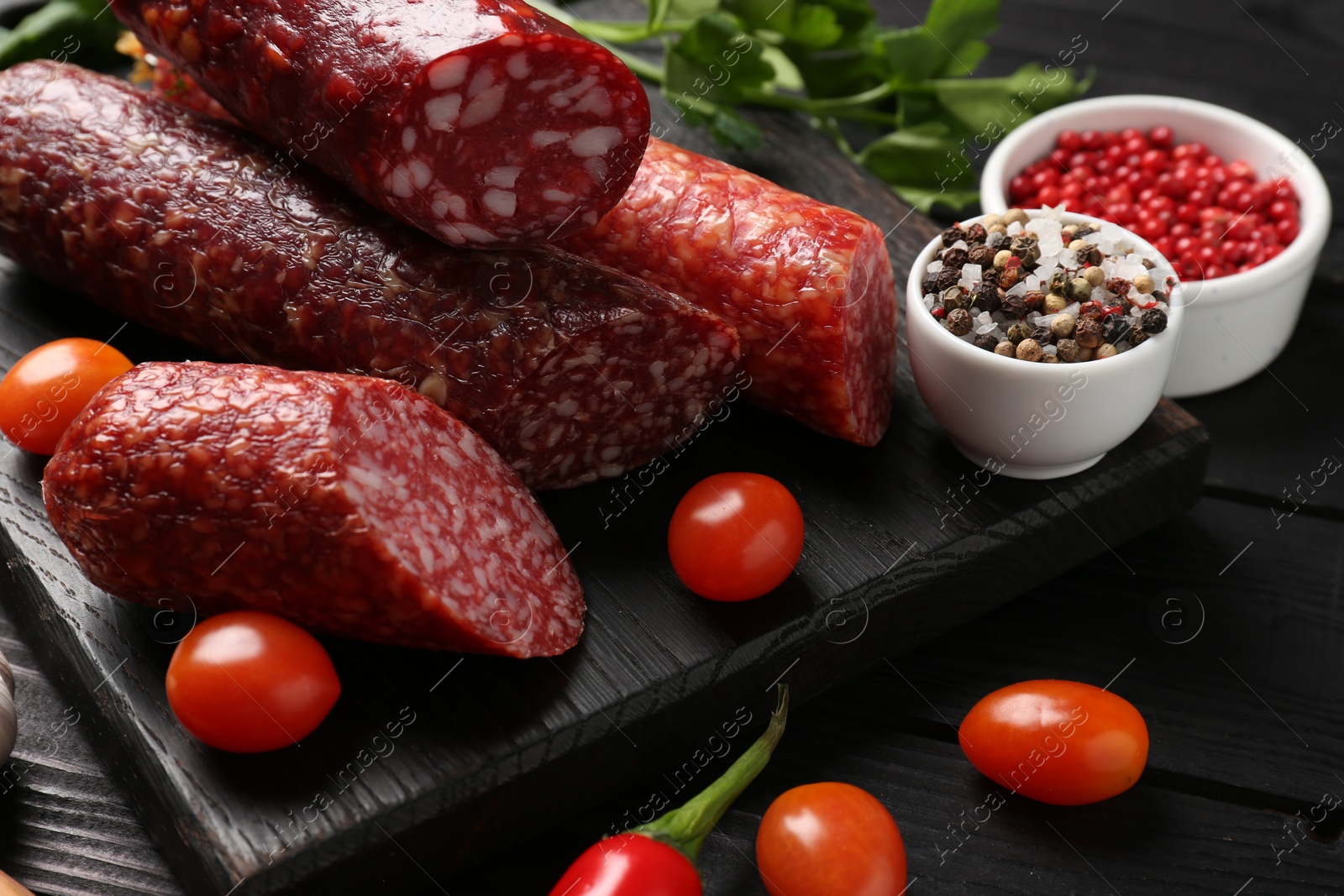 Photo of Different smoked sausages and products s on black wooden table, closeup