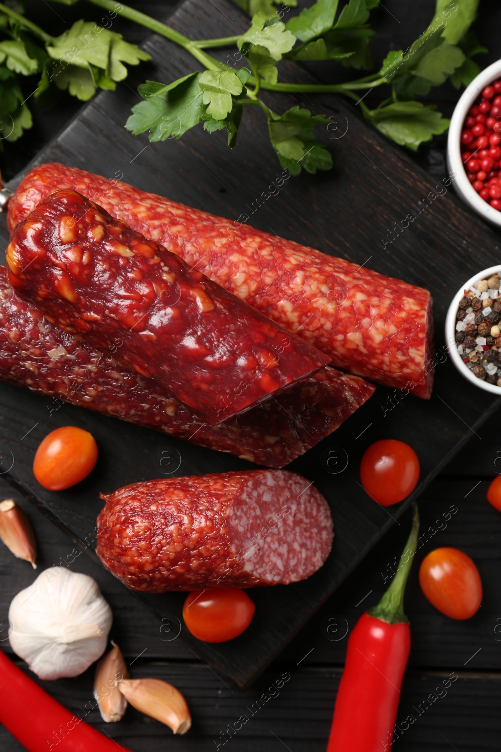 Photo of Different smoked sausages and products on black wooden table, flat lay