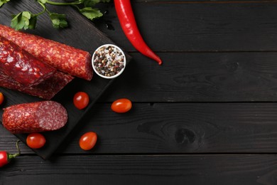 Photo of Different smoked sausages and products on black wooden table, flat lay. Space for text