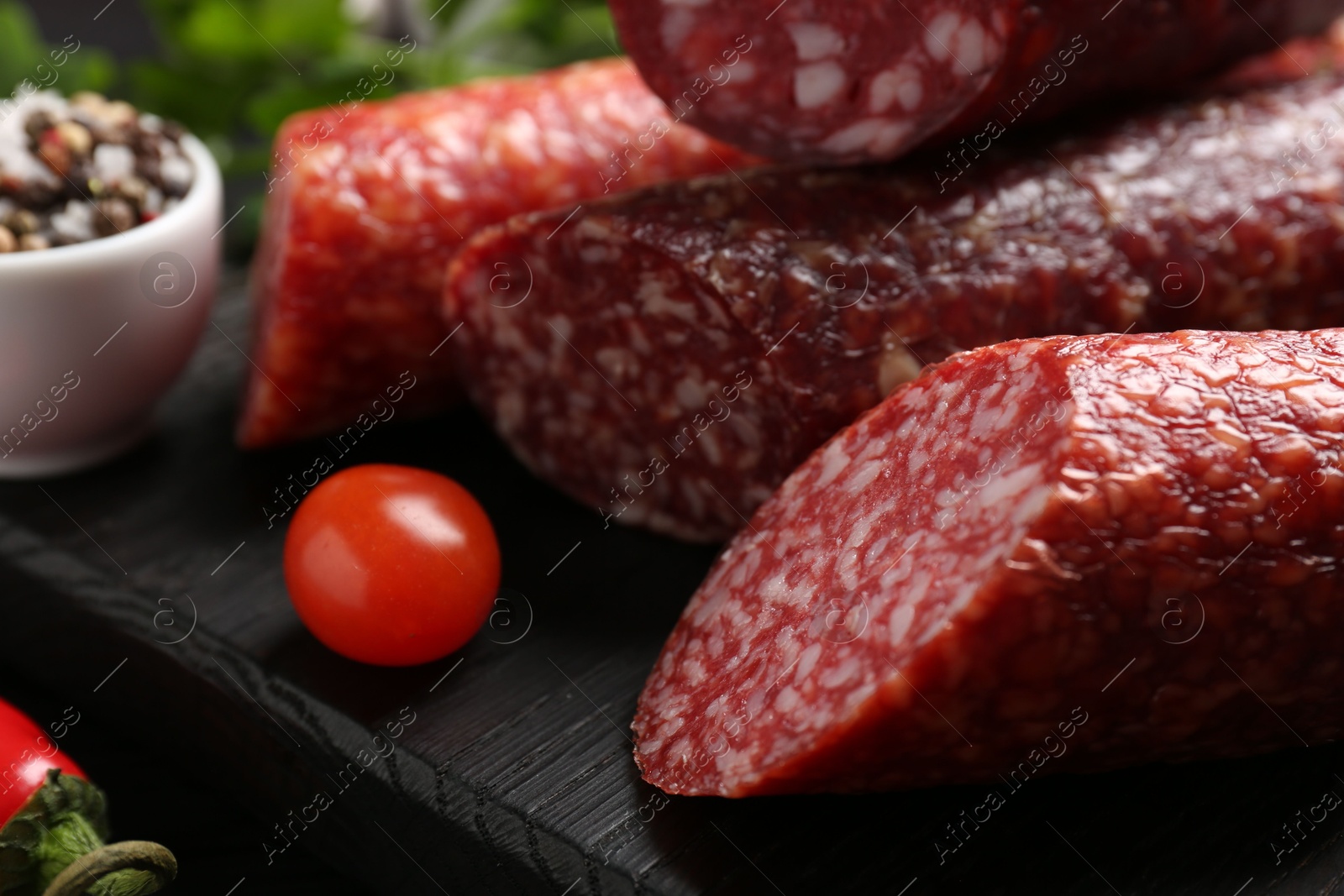 Photo of Different smoked sausages and tomato on black wooden board, closeup