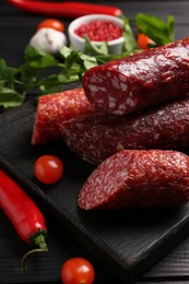 Photo of Different smoked sausages, tomatoes and chili pepper on black wooden table, closeup