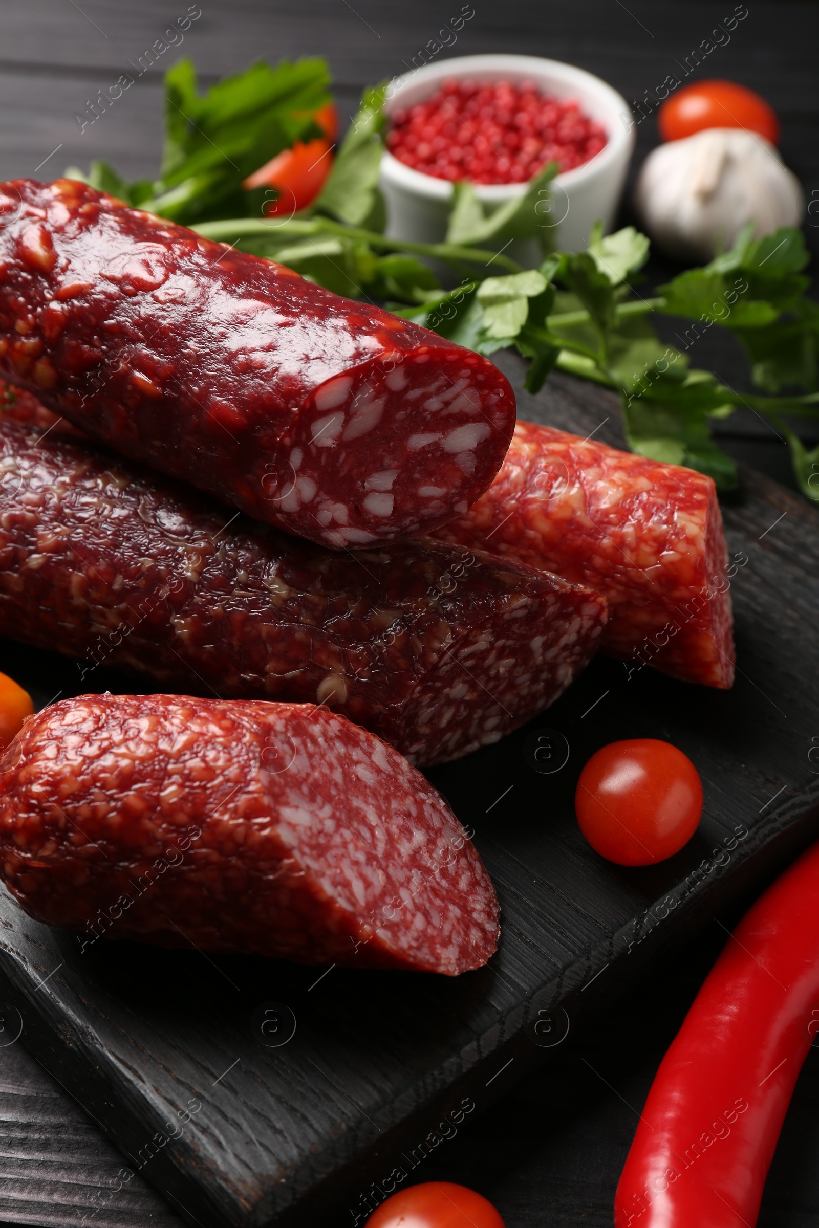 Photo of Different smoked sausages, tomatoes and chili pepper on black wooden table, closeup