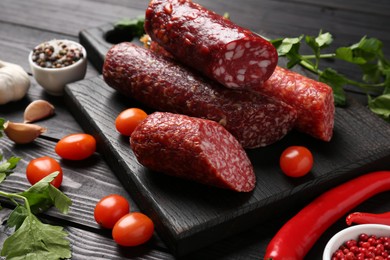 Photo of Different smoked sausages, tomatoes and chili pepper on black wooden table, closeup