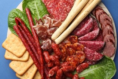 Photo of Different smoked sausages and other snacks on blue background, top view