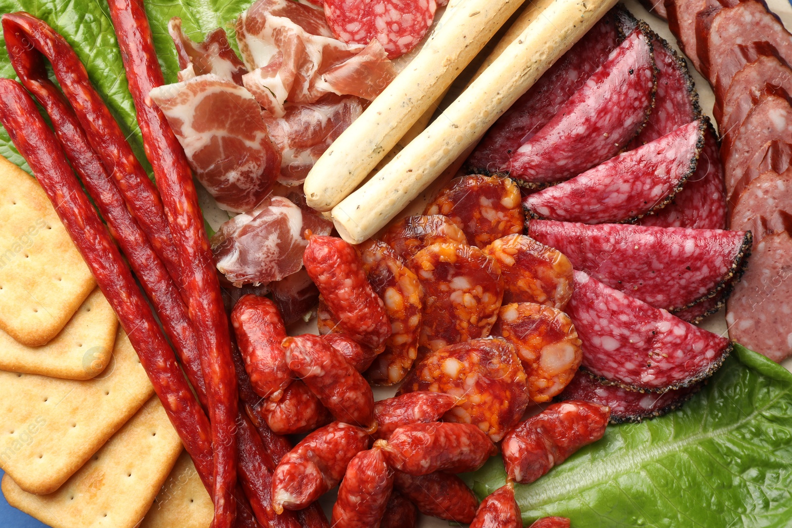 Photo of Different smoked sausages and other snacks as background, top view