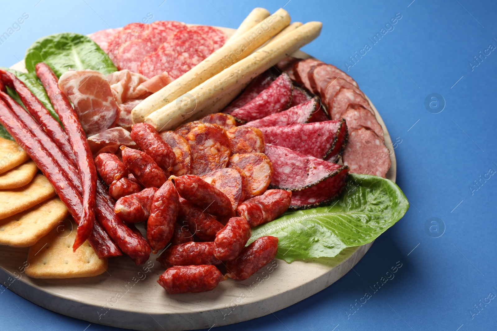 Photo of Different smoked sausages and other snacks on blue background, closeup