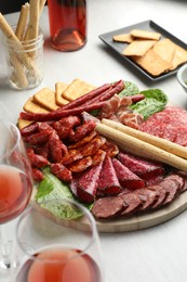 Photo of Different smoked sausages and other snacks served with wine on white table, closeup