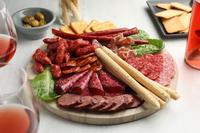 Photo of Different smoked sausages and other snacks served with wine on white table, closeup