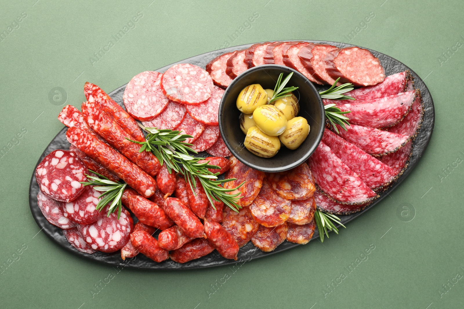 Photo of Different smoked sausages, olives and rosemary on green background, top view