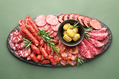 Photo of Different smoked sausages, olives and rosemary on green background, top view