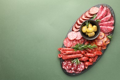 Photo of Different smoked sausages, olives and rosemary on green background, top view. Space for text