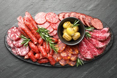 Photo of Different smoked sausages, olives and rosemary on black table, top view