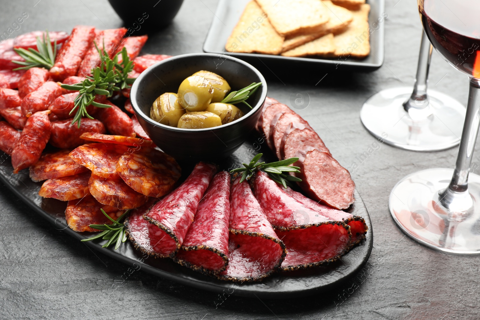 Photo of Different smoked sausages and other snacks served with wine on black table, closeup