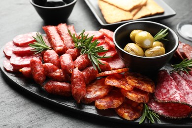 Photo of Different smoked sausages, olives and rosemary on black table, closeup