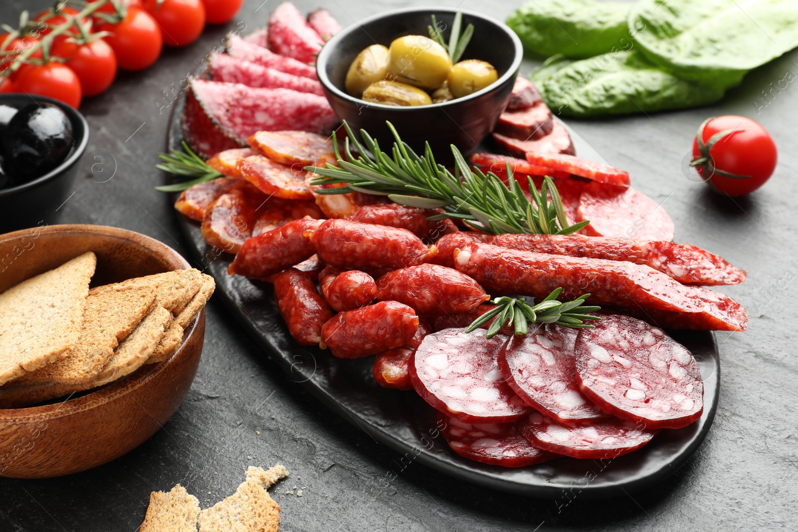 Photo of Different smoked sausages and other snacks on black table, closeup