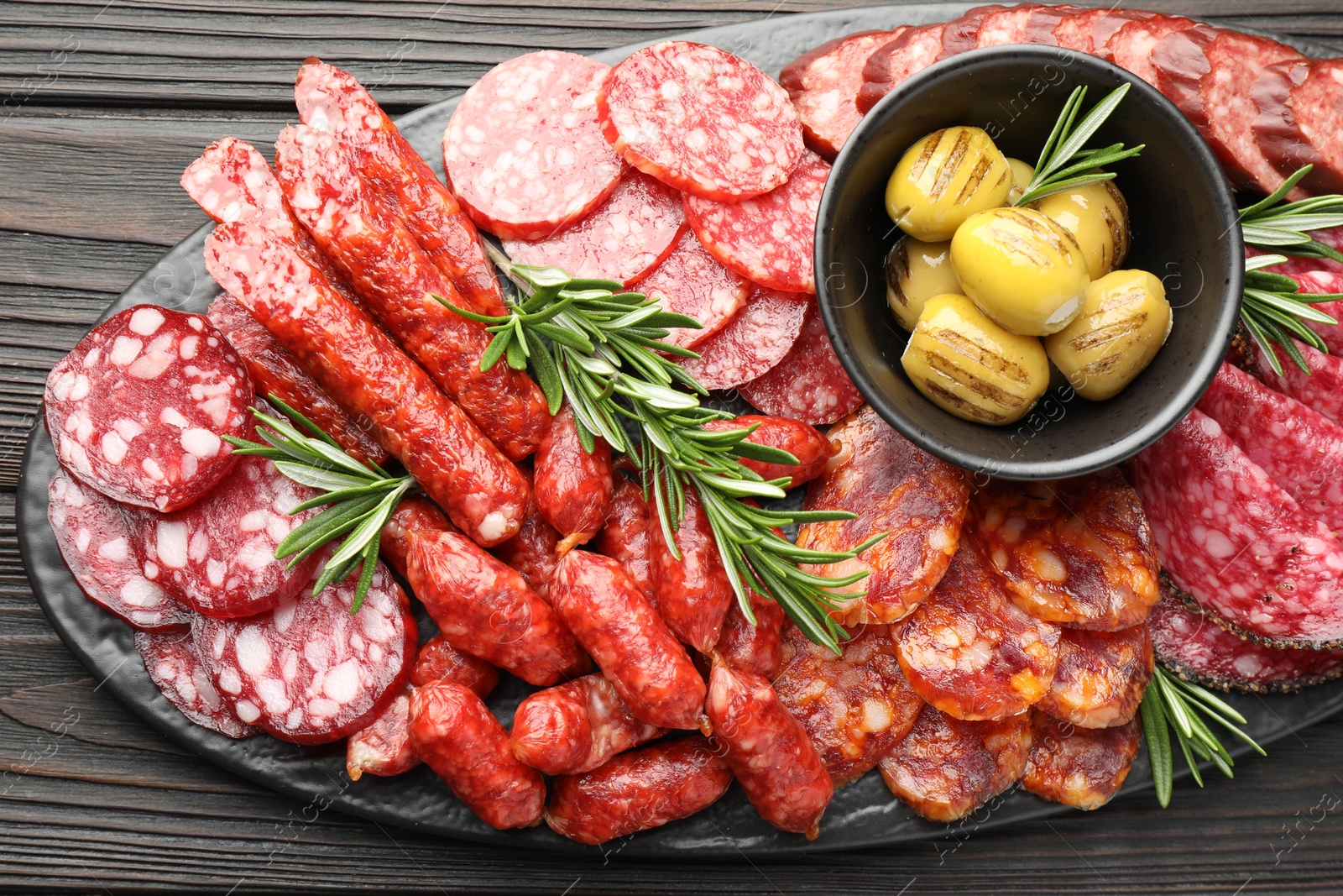 Photo of Different smoked sausages, olives and rosemary on wooden table, top view