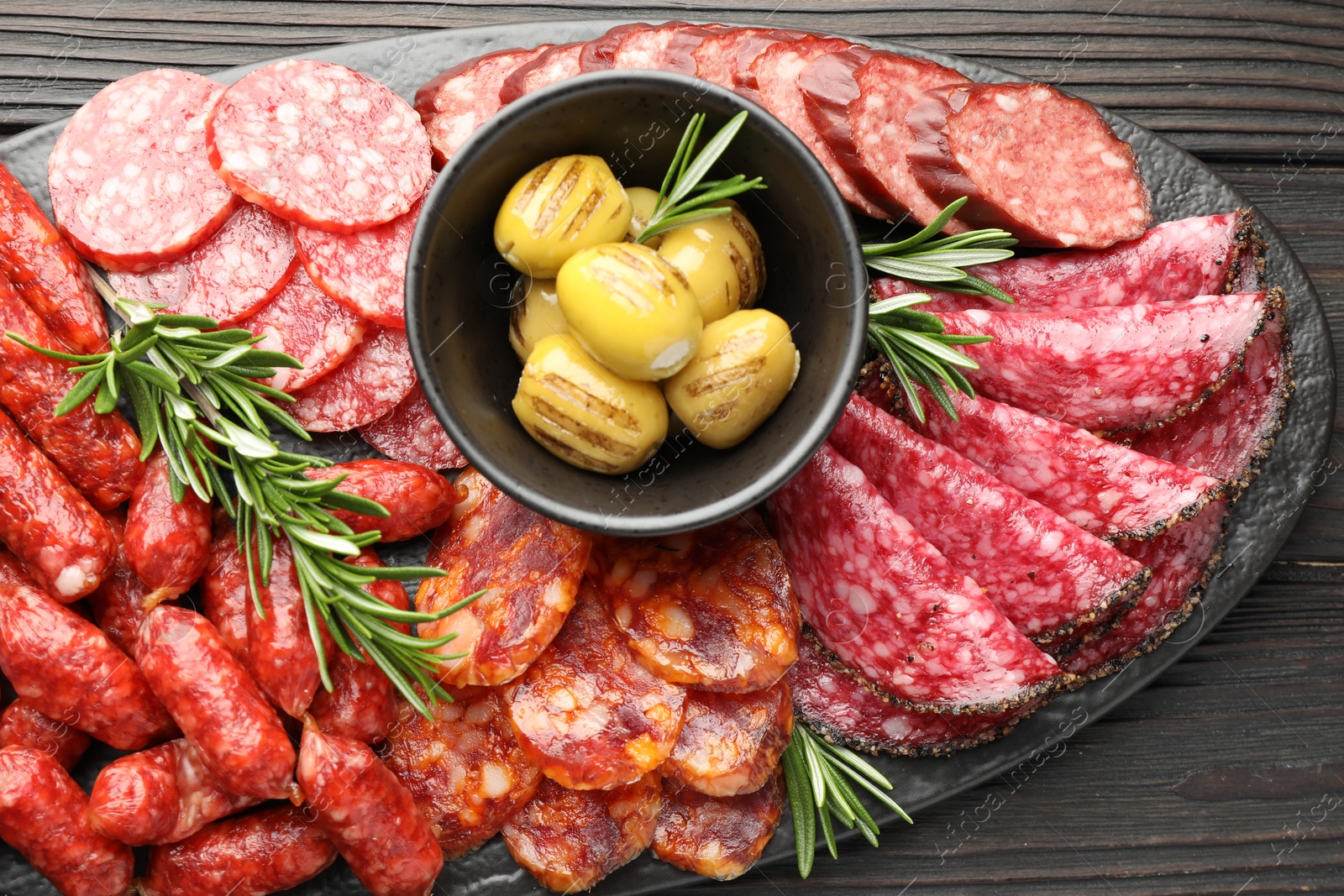 Photo of Different smoked sausages, olives and rosemary on wooden table, top view