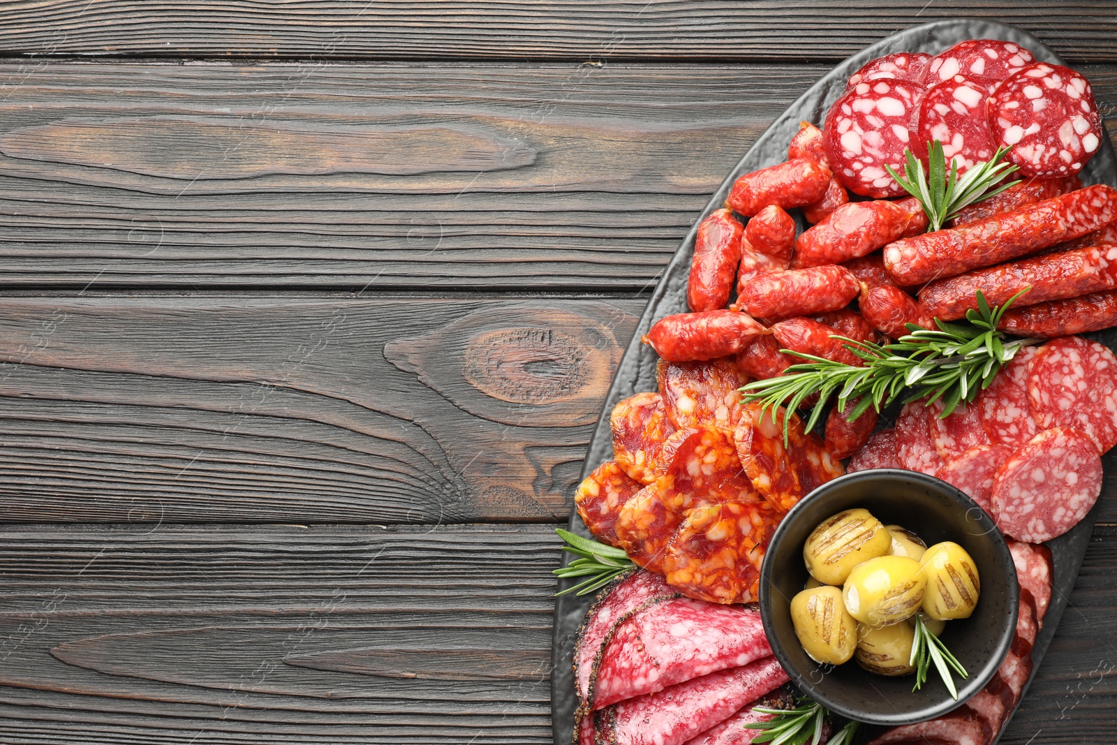 Photo of Different smoked sausages, olives and rosemary on wooden table, top view. Space for text