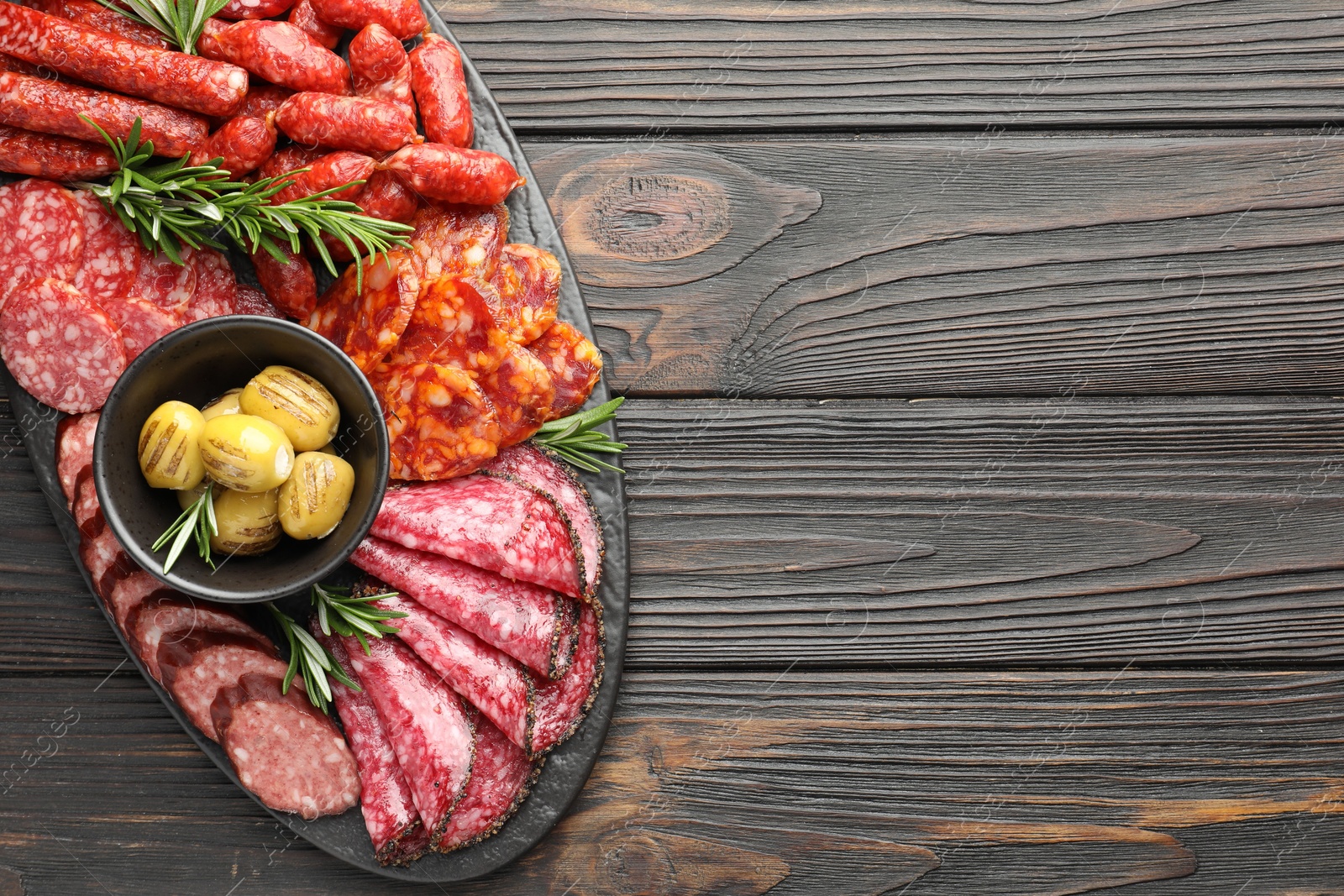 Photo of Different smoked sausages, olives and rosemary on wooden table, top view. Space for text