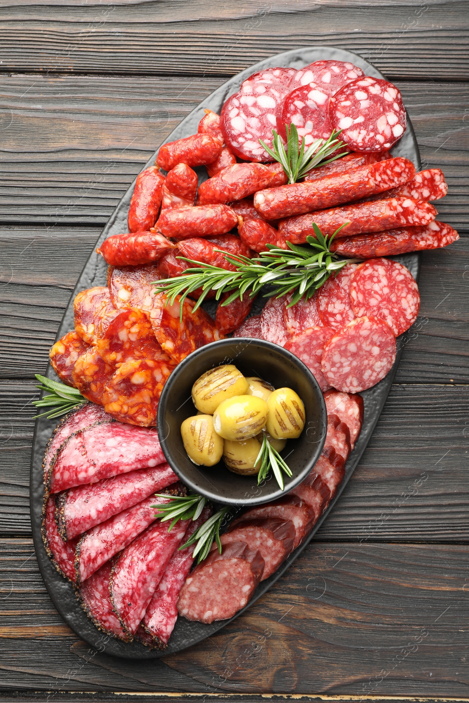 Photo of Different smoked sausages, olives and rosemary on wooden table, top view