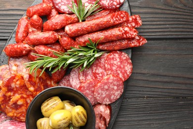 Photo of Different smoked sausages, olives and rosemary on wooden table, top view. Space for text