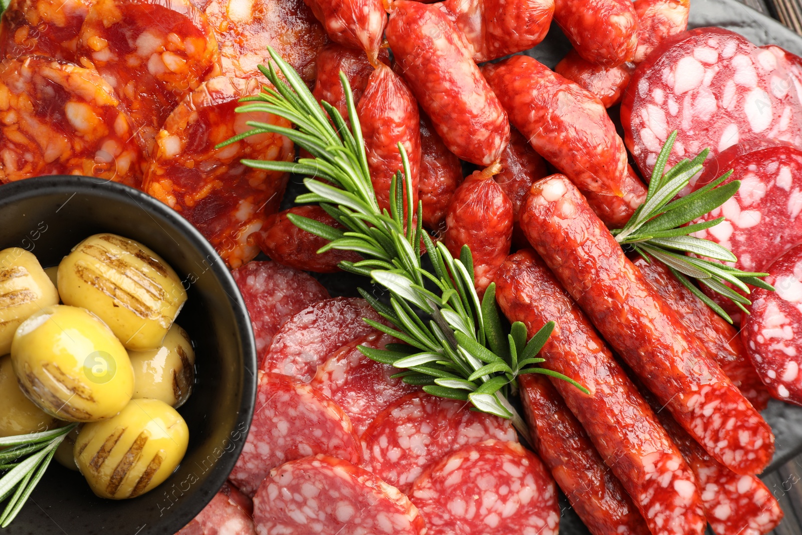 Photo of Different smoked sausages, olives and rosemary on table, top view