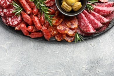 Photo of Different smoked sausages, olives and rosemary on grey table, top view. Space for text