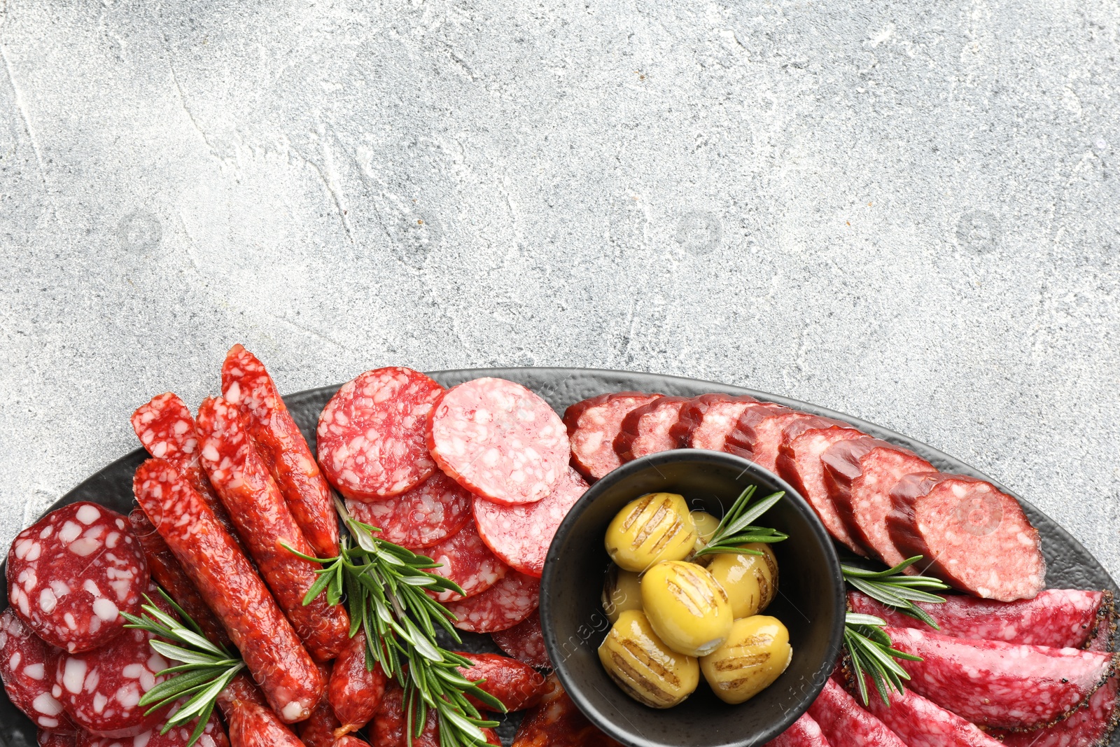 Photo of Different smoked sausages, olives and rosemary on grey table, top view. Space for text