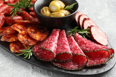 Photo of Different smoked sausages, olives and rosemary on grey table, closeup