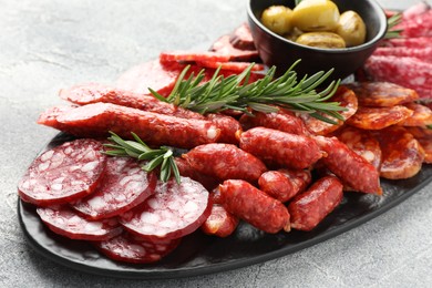 Photo of Different smoked sausages, olives and rosemary on grey table, closeup