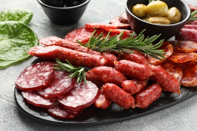 Photo of Different smoked sausages, olives and rosemary on grey table, closeup