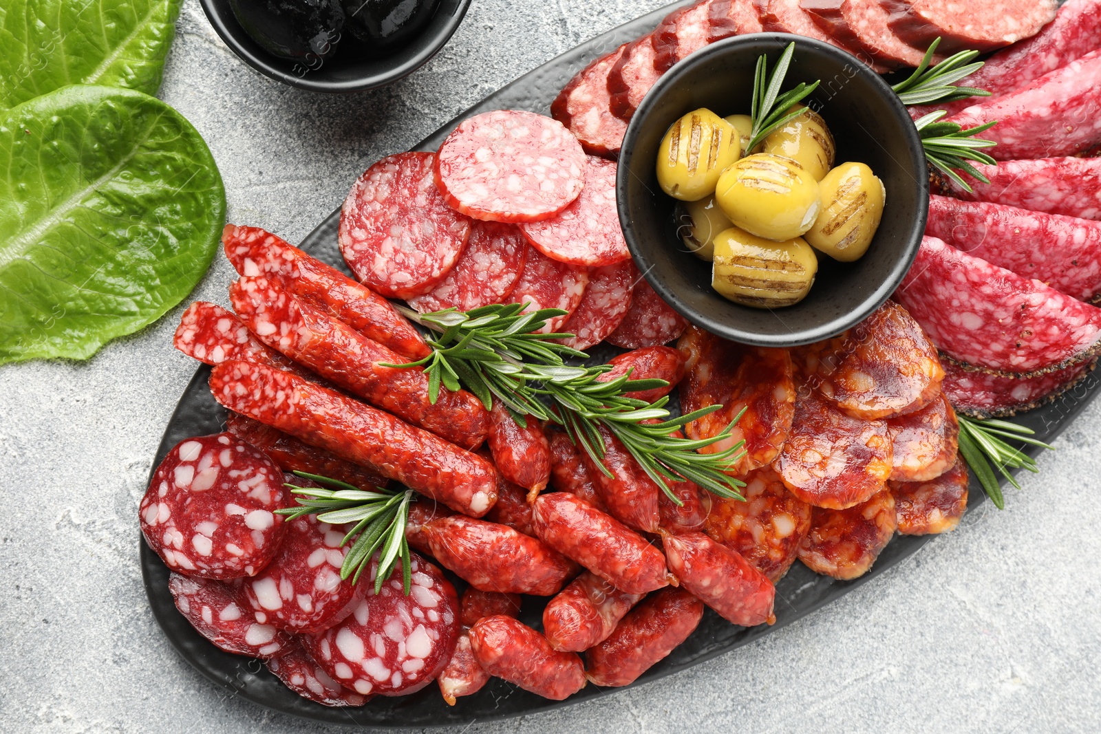 Photo of Different smoked sausages, olives and rosemary on grey table, flat lay