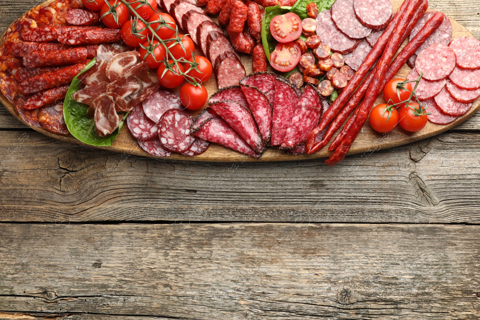 Photo of Different smoked sausages, ham and tomatoes on wooden table, top view. Space for text