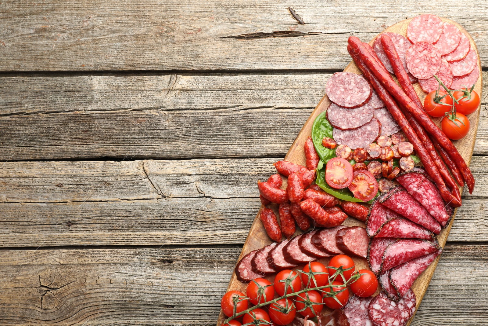 Photo of Different smoked sausages and tomatoes on wooden table, top view. Space for text